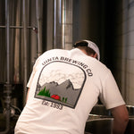 Load image into Gallery viewer, A brewer wearing a t-shirt with a mountain graphic reaches into a brewing kettle
