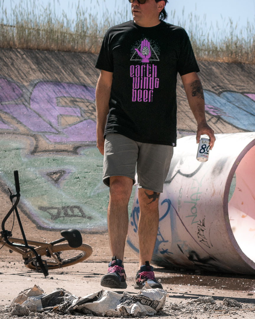 A person  holds a can of beer while walking near a bicycle and a graffiti covered backdrop