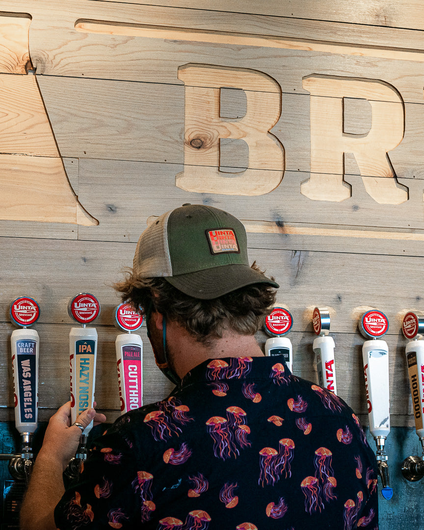 A person wearing a backwards hat and jellyfish shirt pours beer from a draft system